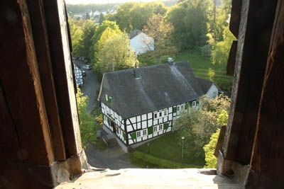 Blick durchs Kirchturmfenster auf das alte Fachwerkpfarrhaus neben der Oberholzklauer Kirche (Quelle: Homepage des ev. Kirchenkreis Siegen)